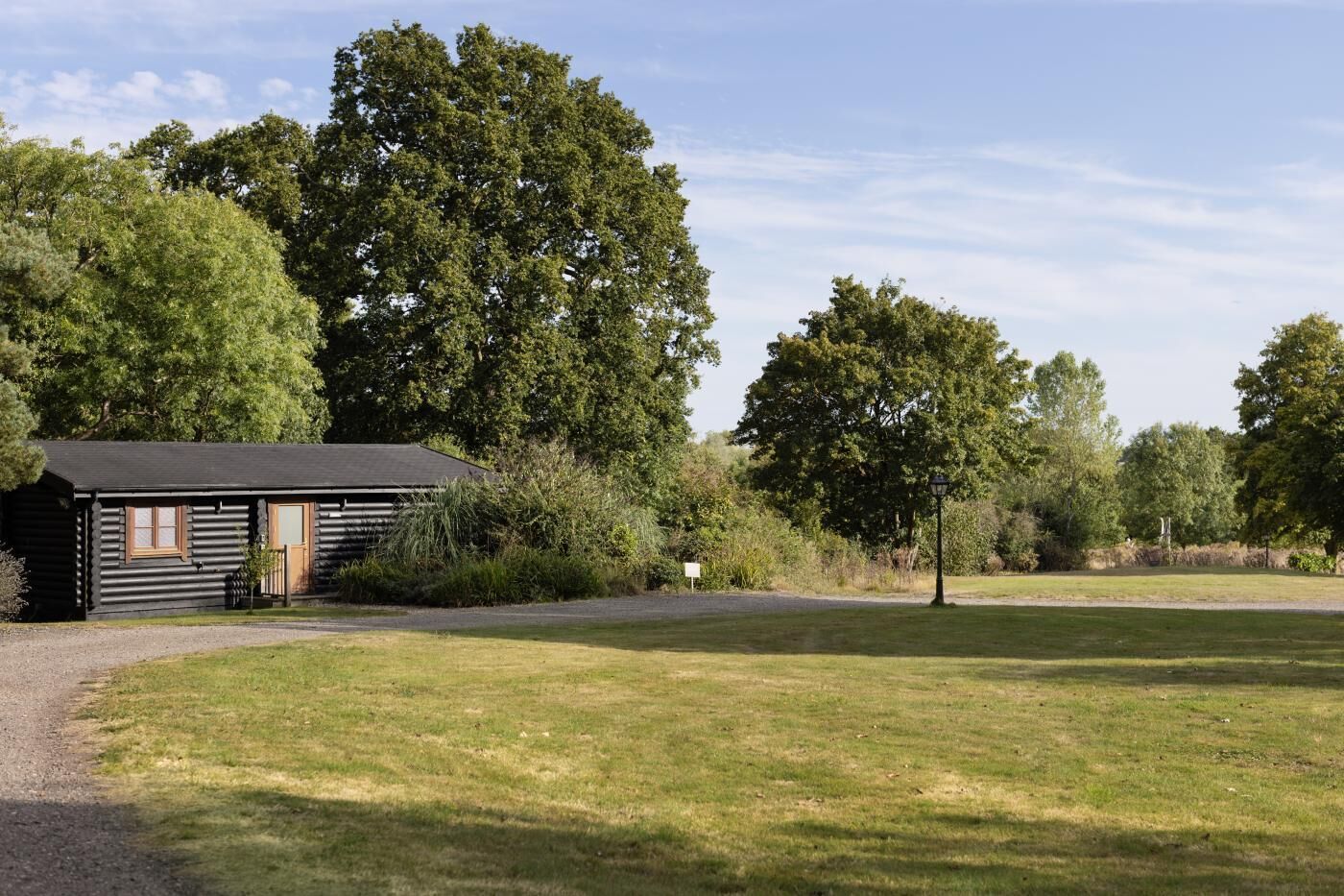 Un chalet rustique avec une allée en gravier, entouré d’une végétation luxuriante et d’arbres.