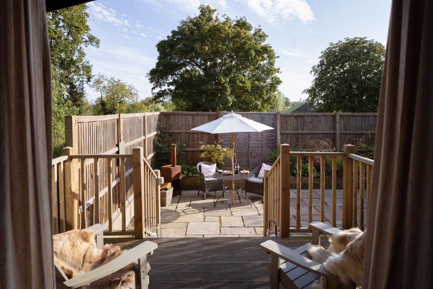 Un espace patio avec une table et des chaises, une clôture en bois et une vue sur les arbres environnants.