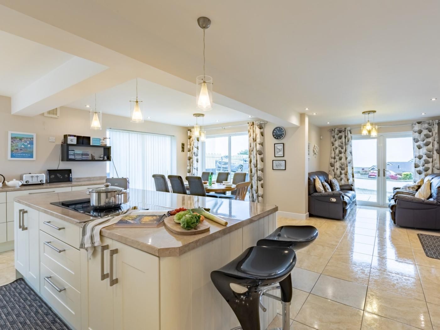 A modern kitchen with a central island, dining area with chairs, and a living room with a sofa.