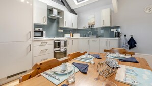 Une cuisine moderne avec des meubles blancs, un puits de lumière et un coin repas comprenant des chaises en bois et une table dressée pour deux personnes.