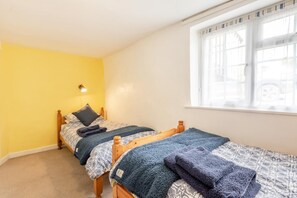 A room with two wooden beds, a window with blinds, and a wall-mounted light. - 2 Bed in Bideford (oc-73954) (Hartland)