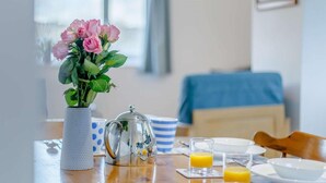 Une table de petit-déjeuner ornée d’un vase rempli de fleurs roses, d’une théière, d’un verre de jus d’orange et d’une tasse à rayures bleues et blanches.