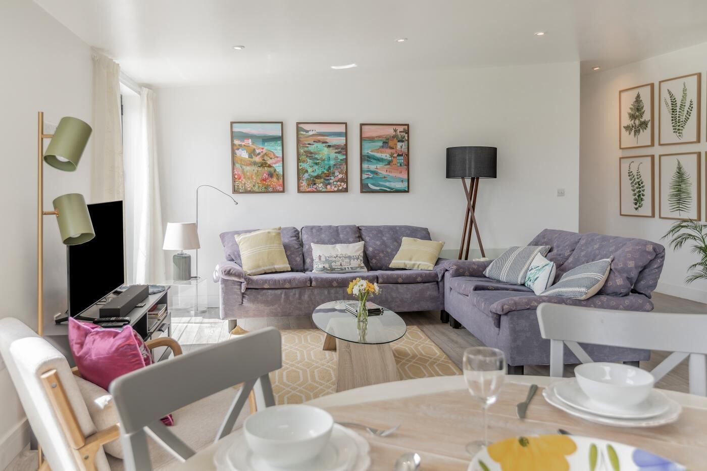 Een moderne woonkamer met een zithoek, een salontafel, een eettafel met stoelen, een televisie en kunstwerken aan de muur.