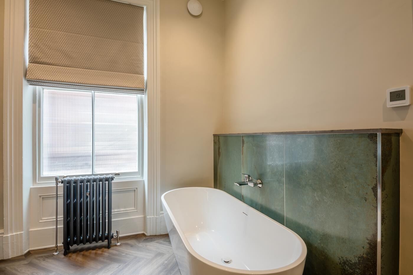 Een badkamer met een bad, een radiator en een raam met zonwering.