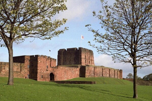 A historic brick castle with a flag, surrounded by a grassy area and trees.