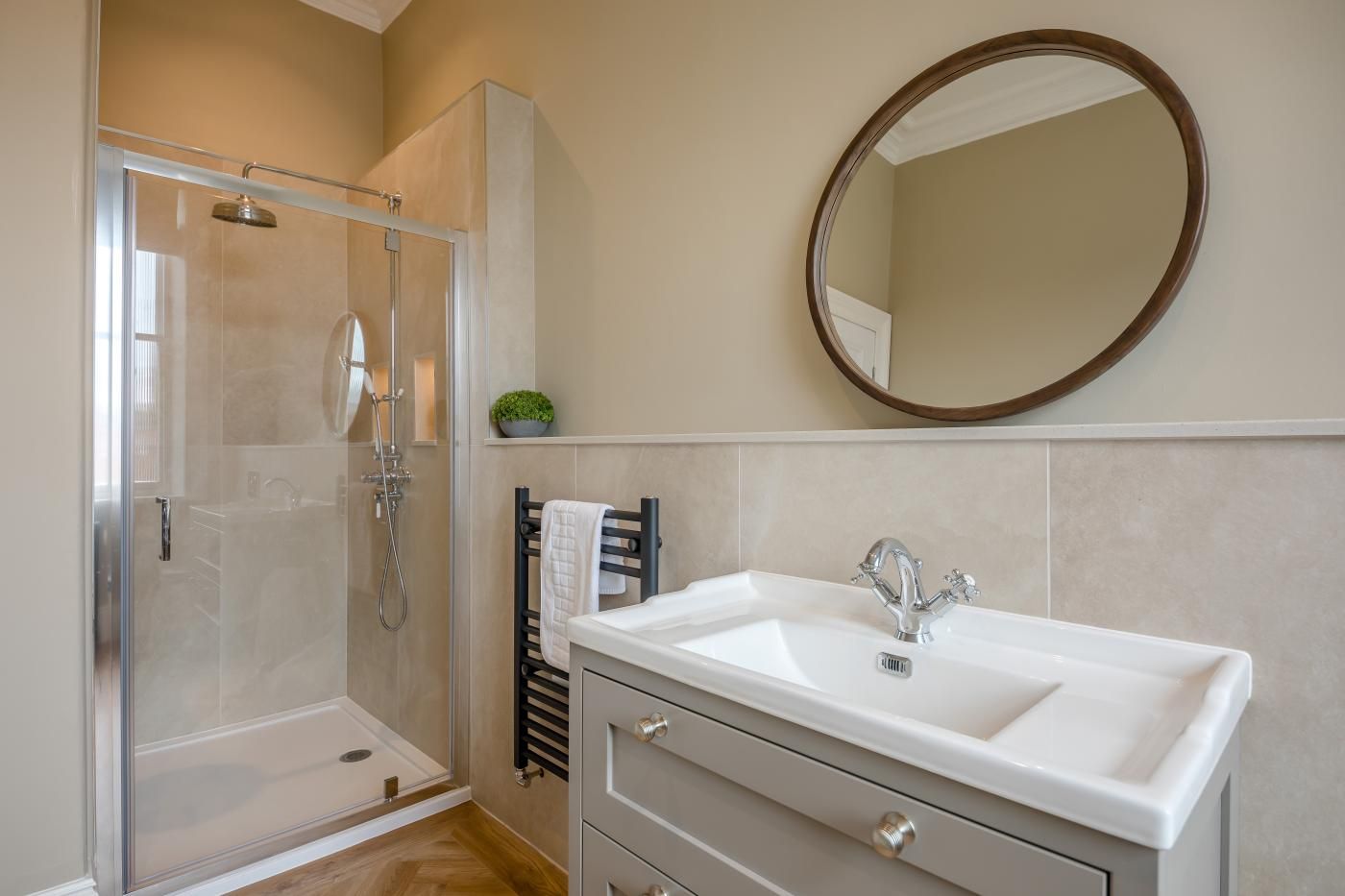 A bathroom with a glass-enclosed shower, a white sink with a modern faucet, and a round mirror on the wall.