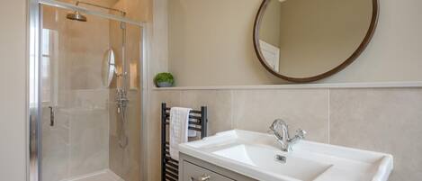 A bathroom with a glass-enclosed shower, a white sink with a modern faucet, and a round mirror on the wall.