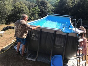 En oppustelig swimmingpool med stige og vandhane, omgivet af en græsplæne med træer.