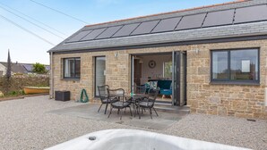 Un edificio de piedra con un patio, un jacuzzi y una zona de comedor con sillas y una mesa.