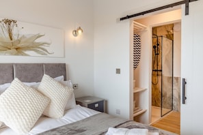 Ein Schlafzimmer mit einem Bett, Kissen, einem Nachttisch, einer Wandleuchte und einer Schiebetür zu einem Duschbereich.