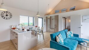 Una cocina moderna con una isla central, un comedor con un sofá azul y una sala de estar con un ventanal grande.