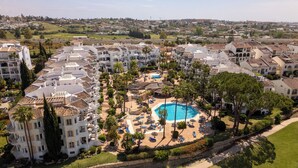 Um resort com piscina central, vários edifícios e vegetação ao redor.