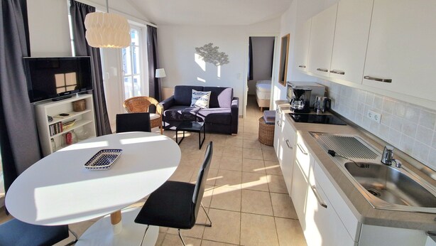 A compact living space with a kitchenette, a dining area, and a seating area with a television and books. - Ferienwohnung mit Balkon in Sonniger Sud-west-lage in Sellin (Sellin)
