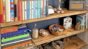 A bookshelf with various books, a book titled 'Atlas of Remote Islands,' and a radio on a shelf. - Coastal Cottage Retreat Steps from the Beach - Pass the Keys (Kirkcudbright)