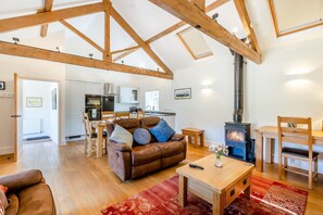 A spacious living area with a high ceiling, wooden beams, a fireplace, a sofa, a dining table, and a kitchen in the background. - 4 Bed in Sherborne (oc-82941) (Ryme Intrinseca)
