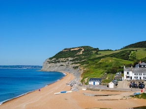 Ein Küstenhotel mit Strand, einem grünen Hügel und blauem Himmel.