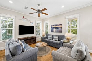 A living room with a flat-screen TV, grey sofas, a coffee table, and a ceiling fan. - Close to Trails and Lakes with Shared Pool (Santa Rosa Beach)
