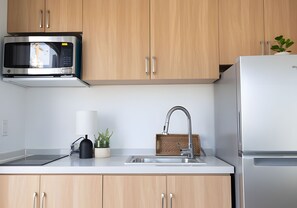 Eine Küche mit Holzausbau, einer Edelstahl-Mikrowelle, einem Spülbecken mit moderner Armatur und einem Kühlschrank.