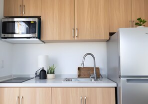 A kitchen with wooden cabinets, a stainless steel microwave, a sink with a modern faucet, and a refrigerator. - Private Duplex Studio Suite with Queen Bed, Kitchenette and Private Bathroom. (Pecos)