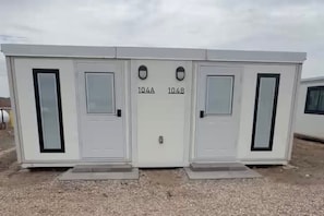A portable building with two doors labeled 104A and 104B, each with a small window. - Private Duplex Studio Suite with Queen Bed, Kitchenette and Private Bathroom. (Pecos)