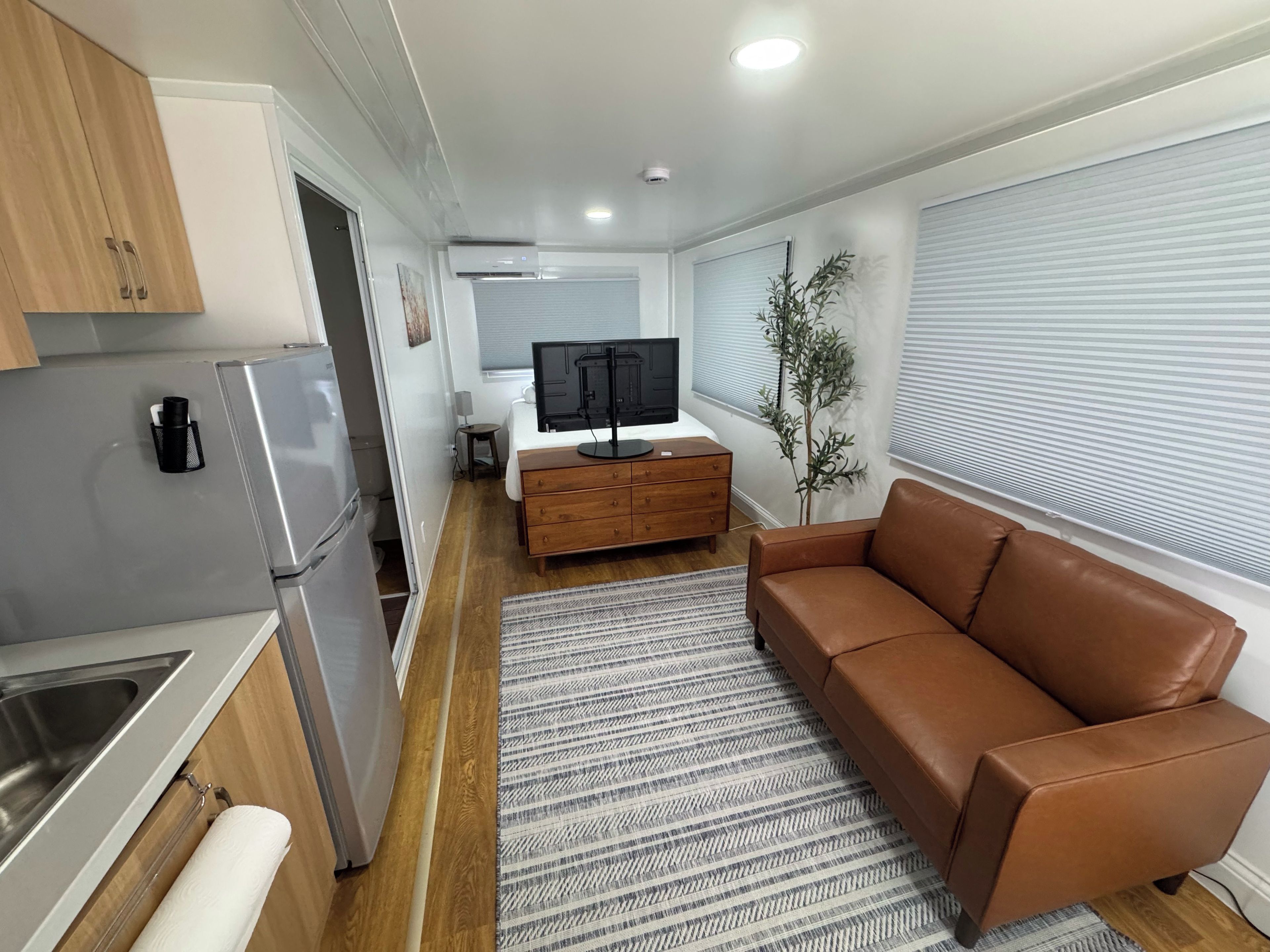 A compact living space with a kitchenette, a brown leather sofa, a TV, and a small side table.