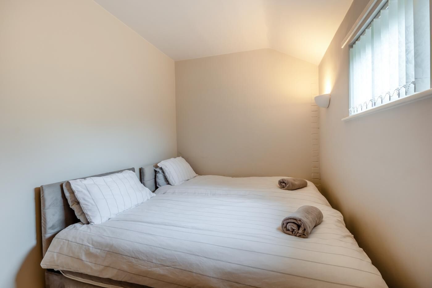 A small, neatly made bed with a headboard, two pillows, and two rolled towels.
