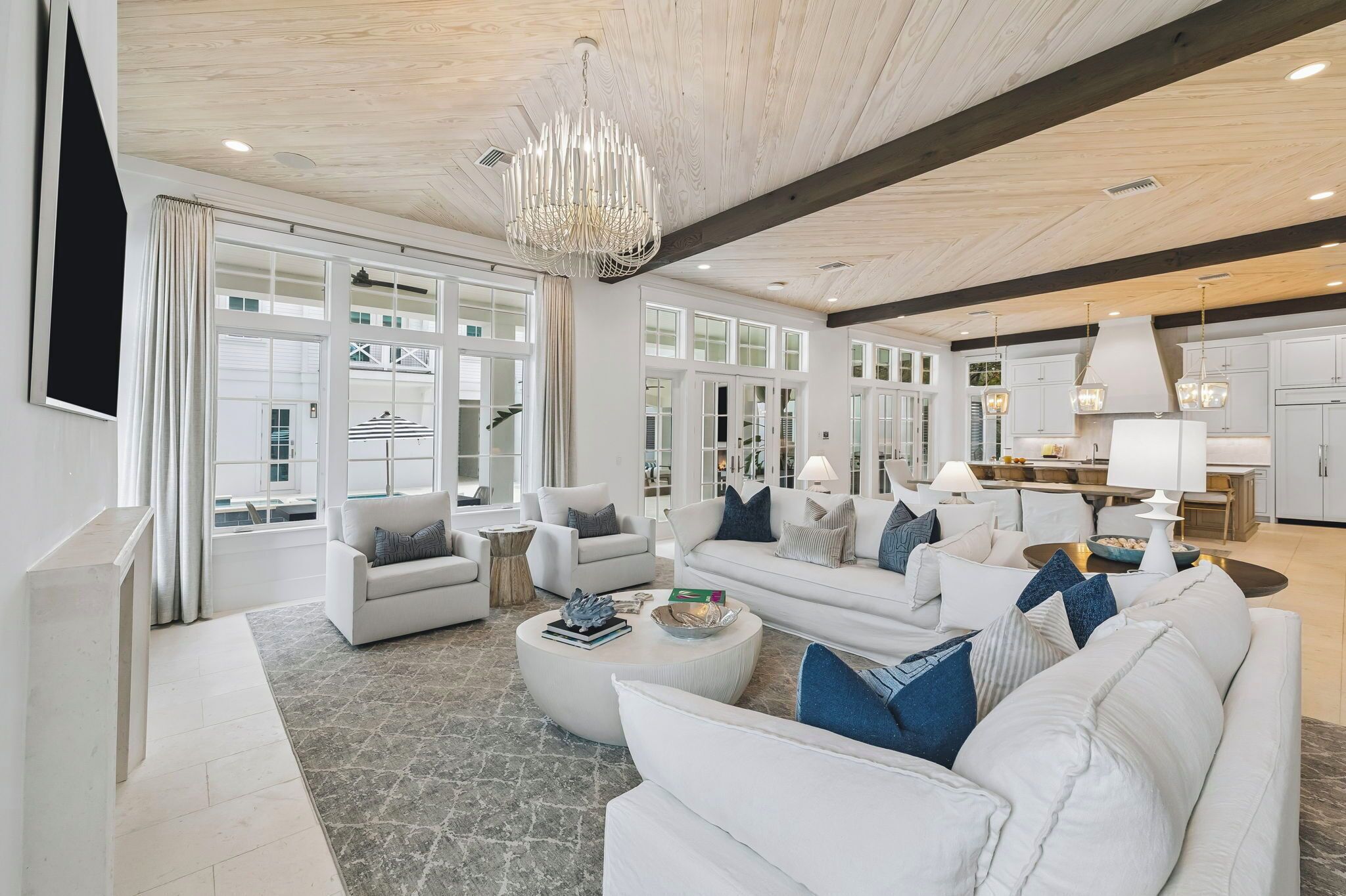A spacious living area with white sofas, a chandelier, and large windows.