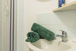 Ein Badezimmer mit einem weißen Waschbecken, einem grünen Handtuch und einer Dusche mit einer weißen Tür.