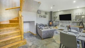A modern living room with a wooden staircase, a fireplace, a sofa, a dining table set for two, and a flat-screen TV mounted on the wall. - 1 Bed in Banff (oc-t42474) (Banff)
