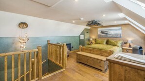 A bedroom with a lofted sleeping area, a wooden bed frame, a green bedspread, a nightstand, a lamp, and a view of the outdoors. - 1 Bed in Banff (oc-t42474) (Banff)