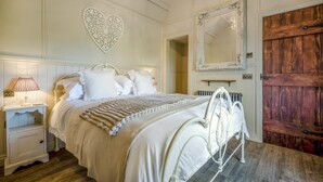 A bedroom with a bed, nightstands, a heart-shaped wall decoration, a mirror, and a wooden door. - 1 Bed in Near Boscastle (oc-f42575) (Forrabury and Minster)