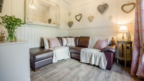 A cozy living room with a leather sofa, decorative heart-shaped wall hangings, a mirror, and a small table with a lamp. - 1 Bed in Near Boscastle (oc-f42575) (Forrabury and Minster)