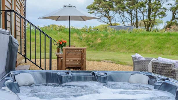A hot tub with a control panel, a wooden chair, a table with a vase of flowers, and a large umbrella. - 1 Bed in Near Boscastle (oc-f42575) (Forrabury and Minster)