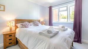 A neatly made bed with white linens, a wooden headboard, and two pillows with floral patterns. There is a nightstand with a lamp and a remote control. - 3 Bed in Westward Ho (oc-s42079) (Westward Ho!)