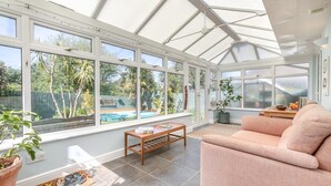 A conservatory with a pool view, a sofa, and a wooden table. - 3 Bed in Westward Ho (oc-s42079) (Westward Ho!)