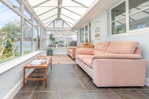 A conservatory with a sofa and a table, large windows, and a view of the outdoors. - 3 Bed in Westward Ho (oc-s42079) (Westward Ho!)