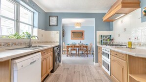 A kitchen with wooden cabinets, a dishwasher, a dining table with chairs, and a view into the dining area. - 3 Bed in Westward Ho (oc-s42079) (Westward Ho!)
