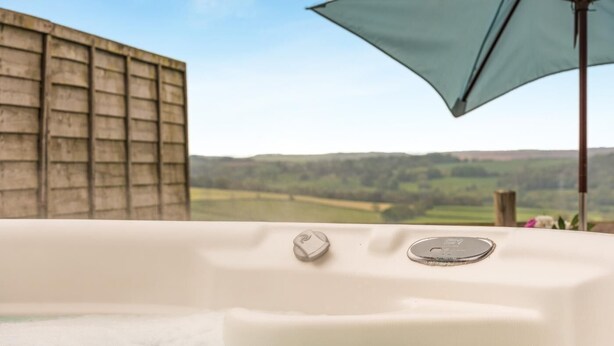 A hot tub with controls, a wooden wall, and a view of green hills.