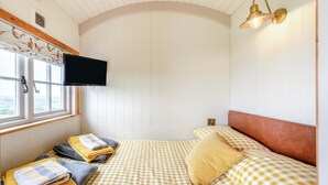 A bedroom with a bed, a TV mounted on the wall, a window, and a ceiling light fixture.
