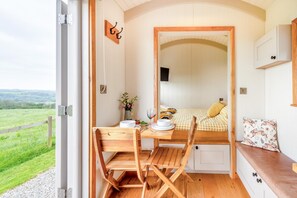 A cozy room with a bed, a dining table, and a chair. There is a view of the outdoors through an open door. - 1 Bed in Bideford (oc-h42651) (Bideford)