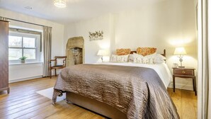 Una camera da letto con un letto grande, un camino, una finestra con tende e due abat-jour.