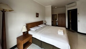 A hotel room with a single bed, a nightstand with a lamp, a wardrobe, and an air conditioning unit. - Townhouse Oak Casa D'Ladera Bandung (Bandung)