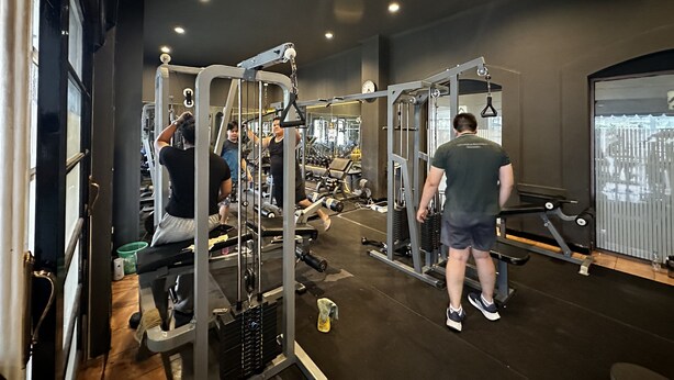 A gym with various exercise machines, a clock on the wall, and a window with blinds. - Townhouse Oak Casa D'Ladera Bandung (Bandung)