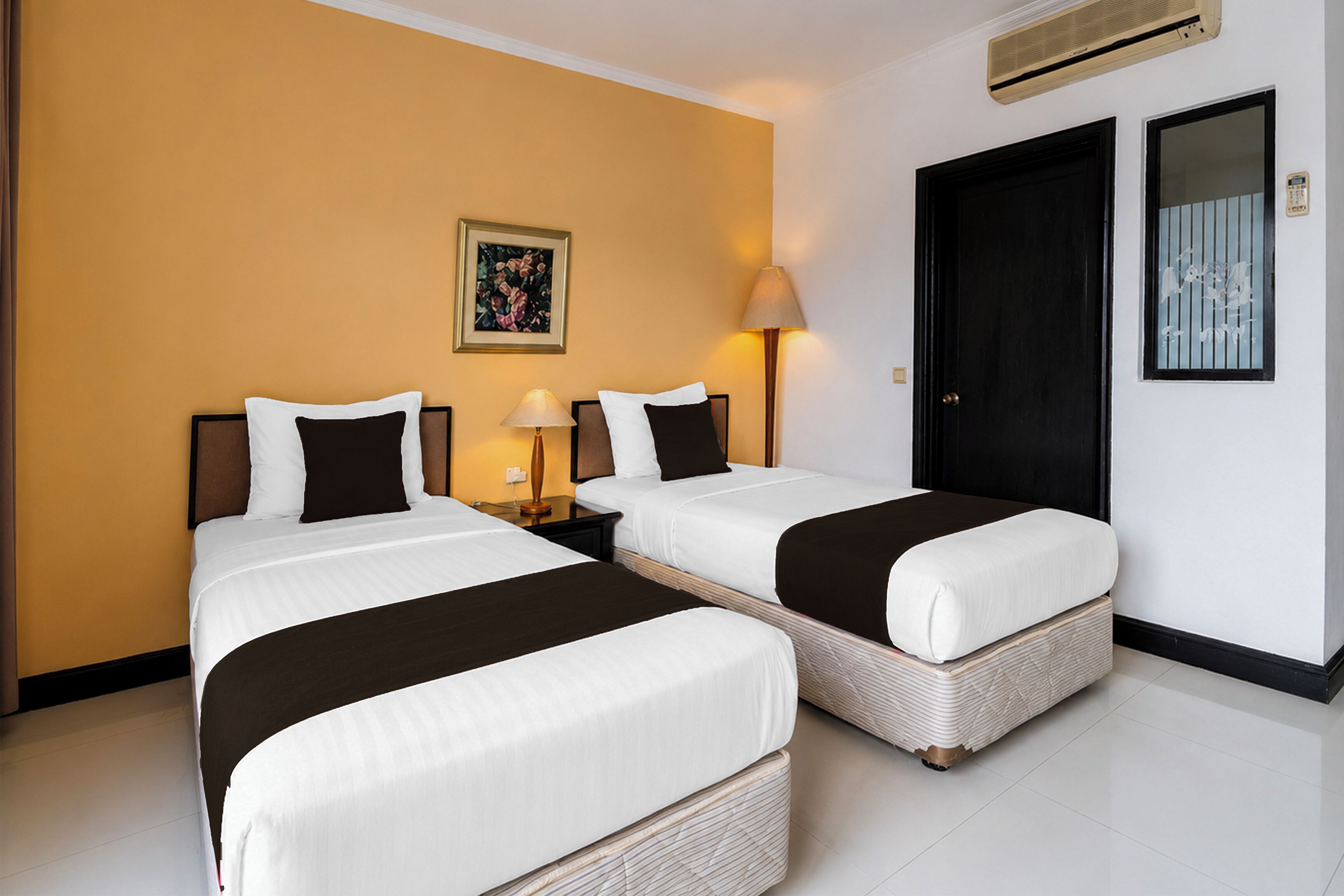 A hotel room with two beds, a painting on the wall, a door with a window, and an air conditioning unit.