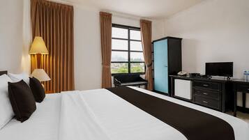 Quarto de hotel com cama, escrivaninha, cadeira, televisão e janela com cortinas.