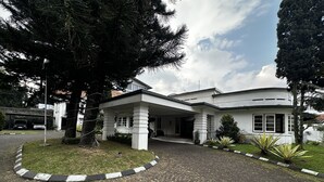 A modern building with a covered entrance, paved driveway, and surrounding greenery. - Townhouse Oak Casa D'Ladera Bandung (Bandung)