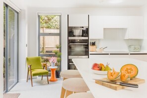 Eine moderne Küche mit großem Fenster, einem Essbereich mit weißem Tisch und einem grünen Stuhl.