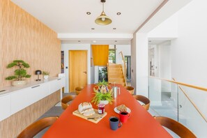 A modern dining area with a long table, chairs, and a central plant arrangement. - 4 Bed in Newlyn (oc-b42667) (Newlyn)