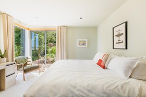 A bedroom with a large bed, a desk, and a chair. There is a window with curtains, a framed picture on the wall, and a plant on the desk. - 4 Bed in Newlyn (oc-b42667) (Newlyn)
