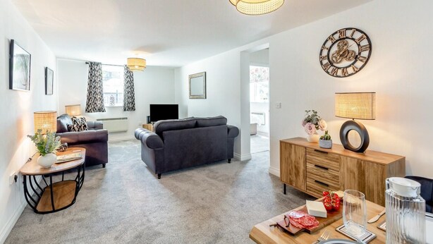 Een moderne woonkamer met een bank, een televisie, een eethoek met een gedekte tafel en een decoratieve klok aan de muur.